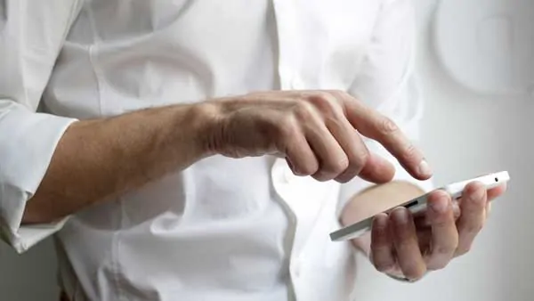 A man in a white work shirt holding a white iPhone