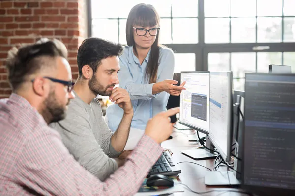 Employees reviewing their work on several computer screens