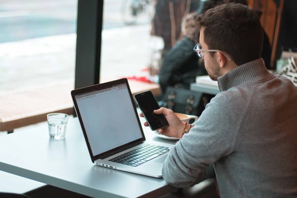 Man in turtle neck sitting in a cafe with his iPhone and Macbook